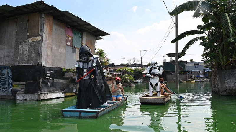 Fotografija: Vaški oficir, oblečen v lik Dartha Vaderja, iz filmske franšize Vojna zvezd, pluje na majhnem čolnu s katerim dostavlja hrano in obleke prebivalcem v poplavljeni vasi Artex v Malabonu na Filipinih. FOTO: Ted Aljibe/Afp