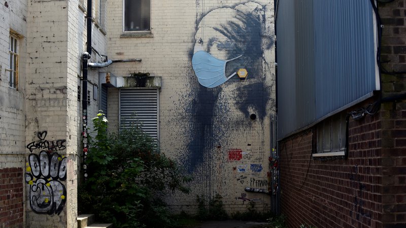 Fotografija: Starejša Banksyjeva umetnina Dekle s preluknjanim bobničem v Bristolu je v času koronakrize dobila dodatek, zaščitno masko čez nos in usta. FOTO: Rebecca Naden/Reuters