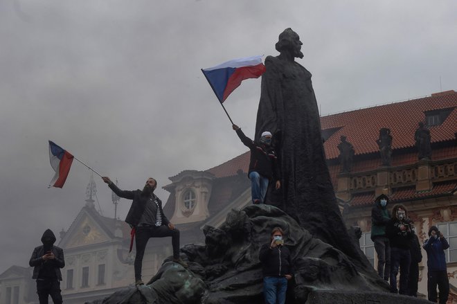 Protestniki v nedeljo zvečer z zastavami stojijo na kipu Jana Husa v Pragi, medtem ko na stotine demonstrantov protestira proti novim vladnim ukrepom vlade za zajezitev koronavirusa. FOTO: Michal Cizek/AFP