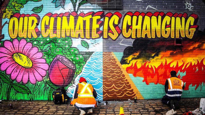 Fotografija: Ulična umetnika barvata zid, ki stoji nasproti prizorišča podnebne konference Združenih narodov v Glasgowu. FOTO: Andy Buchanan/AFP
