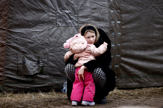 Ženska, ki beži pred rusko invazijo na Ukrajino, objema otroka v začasnem taborišču v Przemyslu. FOTO: Yara Nardi/Reuters
