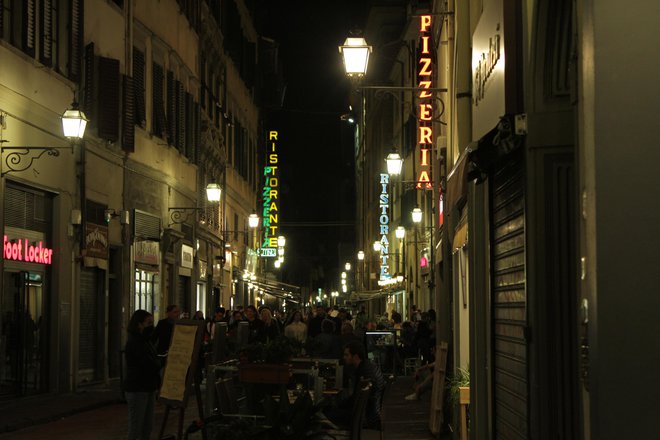 Ulice v osrčju Firenc se svetlikajo pod gosto prepredenimi napisi oštarij, picerij in barov. Ker se večinoma odpirajo šele okoli šeste zvečer, je v njih živahno pozno v noč. FOTO: Mateja Toplak
