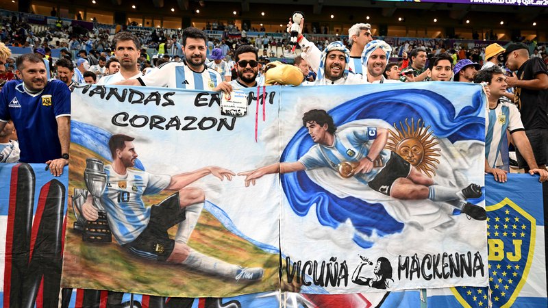 Fotografija: Argentinski navijači so med tekmo s Hrvaško povezali legendarna nogometaša z zastavo: levo Lionel Messi, desno Diego Maradona. FOTO: Manan Vatsyayana/AFP
