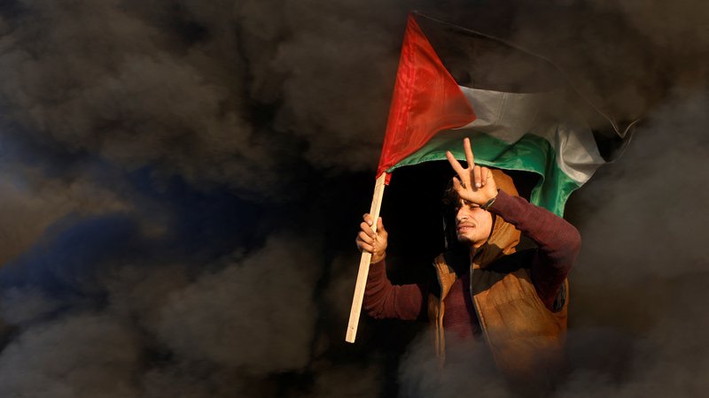 Fotografija: Palestinec drži palestinsko zastavo med spopadi z izraelskimi silami v bližini meje med Izraelom in Gazo vzhodno od mesta Gaza. Foto: Mohammed Salem/Reuters
