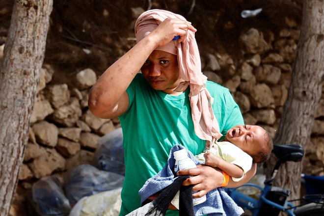 Ena od migrant na Lampedusi drži v naročju otroka. FOTO: Yara Nardi/Reuters