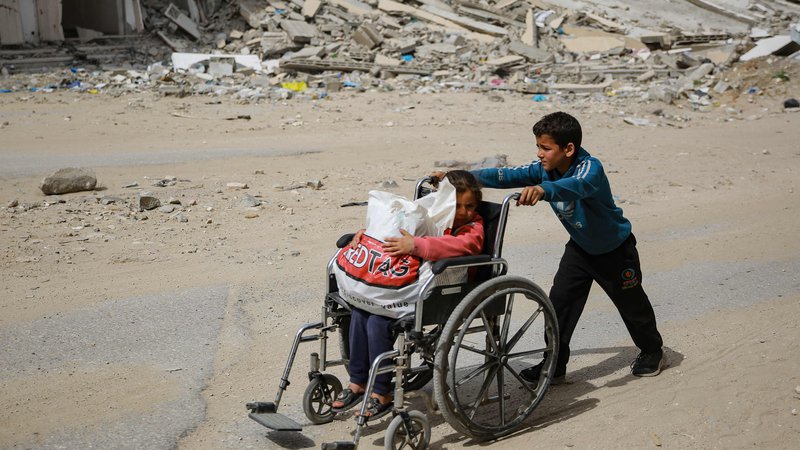 Fotografija: Deček potiska deklico na invalidskem vozičku mimo porušene stavbe v Gazi. Dostave nujno potrebne dobrodelne pomoči v glavnem ovira Izrael, ki ga je Meddržavno sodišče (ICJ) v četrtek pozvalo, da mora brez odlašanja zagotoviti nujno pomoč prebivalcem Gaze. Ob tem je opozorilo na hudo lakoto v palestinski enklavi, ki je že skoraj pol leta tarča nenehnih izraelskih napadov. Foto: Afp