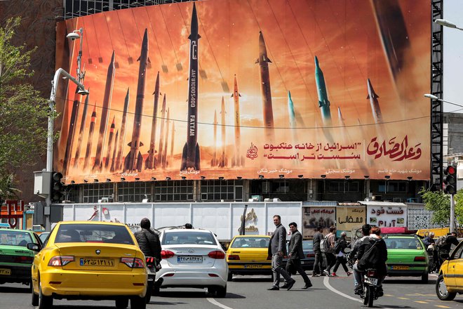 Motoristi se vozijo mimo plakata z uporabljenimi iranskimi balističnimi raketami z napisom v arabščini Častna obljuba in v perzijščini »Izrael je šibkejši od pajkove mreže«. FOTO: Atta Kenare/AFP