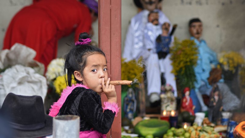 Fotografija: Triletna deklica kadi cigaro med praznovanjem svetega Simona v gvatemalskem mestu San Andres. Na tisoče tamkajšnjih prebivalcev verjame, da svetnik ljudem pomaga najti delo, reši družinske težave in zdravi bolezni. FOTO: Orlando Estrada/AFP