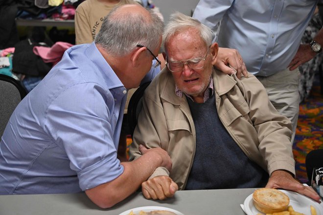 Premier Scott Morrison tolaži 85-letnega Owena Whalana, ki s eje zatekel v evakuacijski center. FOTO: Peter Parks/Afp