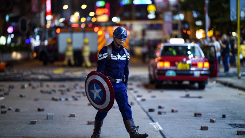 Fotografija: Moški, ki nosi kostum Captain America, hodi po ulici, ko se protestniki zbirajo v bližini policijske postaje v Hongkongu. Hongkong je pretreslo sveže nasilje, ko je več deset tisoč protestnikov ponovno stopilo na ulice, tokrat zaradi prepovedi mask za obraz. FOTO: Mohd Rasfan/AFP