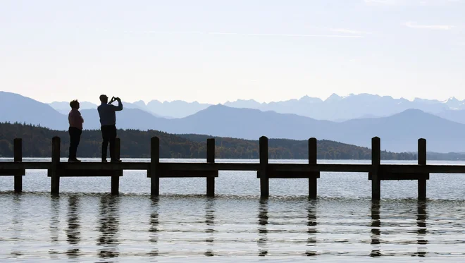 People take a photo of the Alps from a footbridge of the lake Starnberg in front of the Alp mountains near the small Bavarian village of Starnberg, southern Germany, during nice autumn weather with temperatures by 15 degrees on October 17, 2019. (Photo by Christof STACHE / AFP)