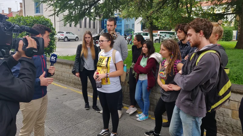 Fotografija: Študentka s plastenko, v kateri je imela črnilo za volilno skrinjico, in skupina študentskih protestnikov daje izjavo za medije.