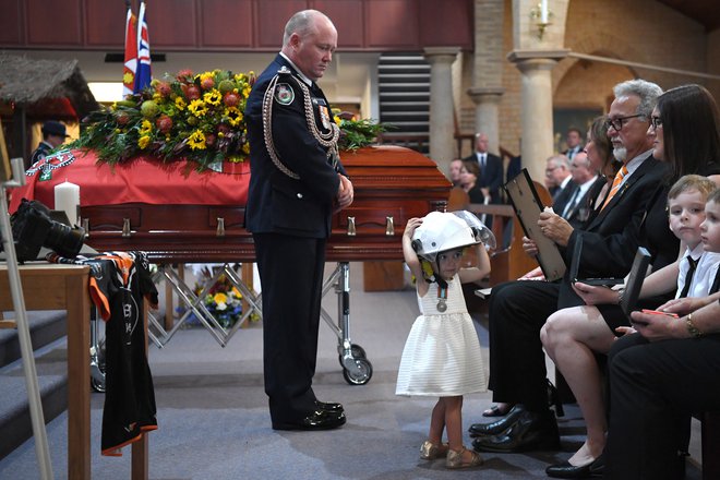 Charlotte, hčerka prostovoljnega gasilca Andrewa O'Dwyerja, ki se je smrtno ponesrečil med gašenjem požarov in je postal ena od petindvajsetih dosedanjih žrtev, je danes na očetovem pogrebu nosila njegovo gasilsko čelado. FOTO: Stringer/ Reuters