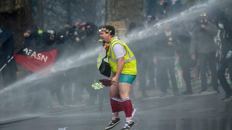 Fotografija: Člana francoskega protivladnega gibanja Rumeni jopiči je v francoskem mestu Nantes namočil policijski vodni top, med stavko zaradi vladne pokojninske reforme. FOTO: Loic Venance/Afp
 