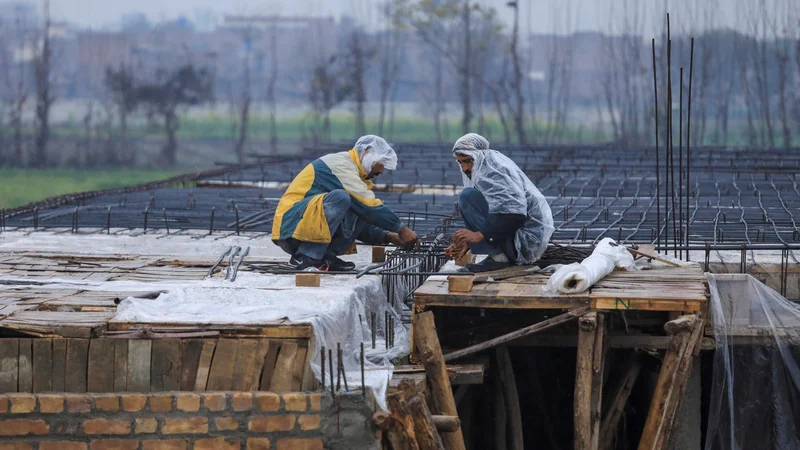 Fotografija: Delavci na prostem so toploto iskali v plastičnih palerinah. FOTO: Fayaz Aziz/Reuters