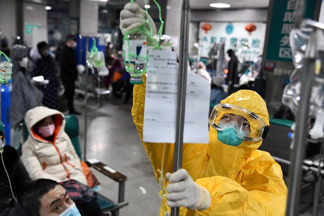 Zdravstveni delavec v zaščitni obleki namešča kapalno vrečko pacientu v bolnišnici v Wuhanu. FOTO: Reuters