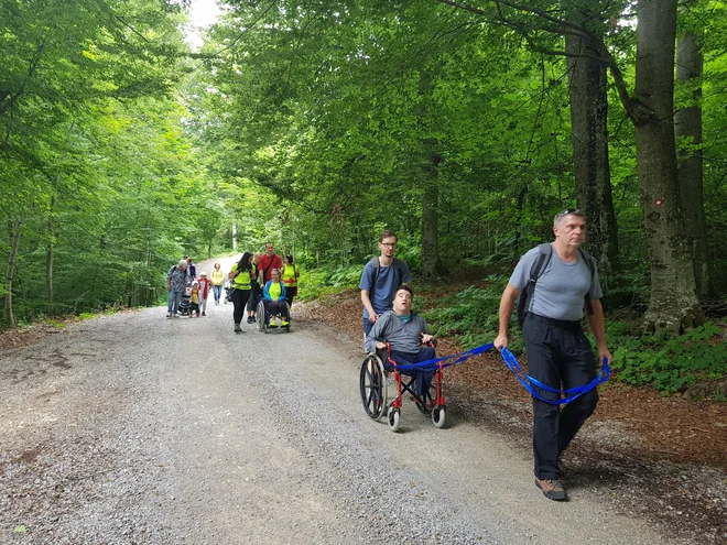 Za pomoč pri vzpenjanju gibalno oviranih sta potrebna dva prostovoljca, eden potiska in drugi vleče voziček s pomočjo vlečne vrvi. Foto Arhiv PZS