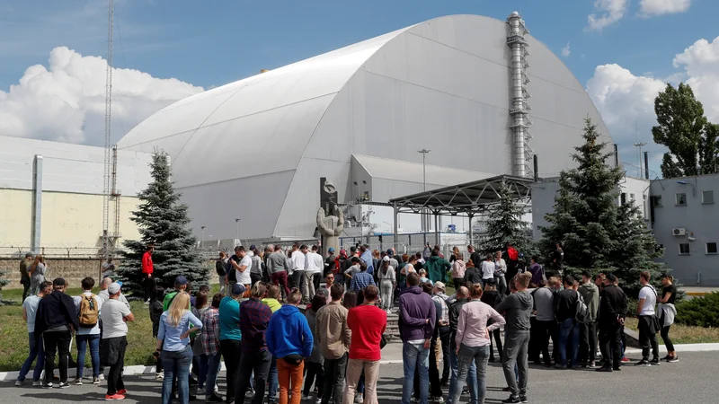 Obiskovalci stojijo pred novim sarkofagom, s katerim so prekrili poškodovani četrti reaktor černobilske jedrske elektrarne. FOTO: Reuters