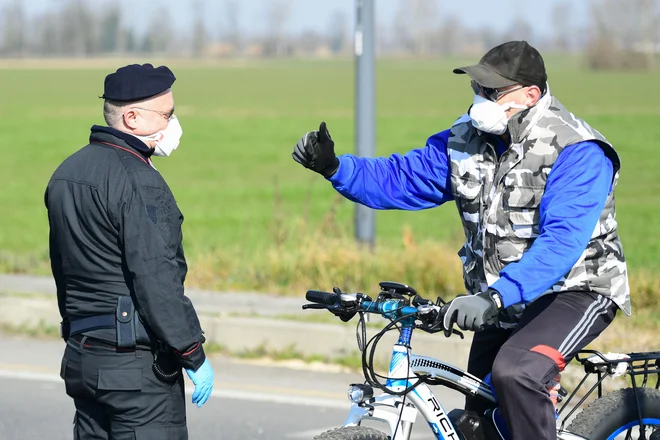 Italijanski karabinjer in prebivalec območja blizu Milana, kjer je več mest v karanteni. FOTO: Miguel Medina/AFP