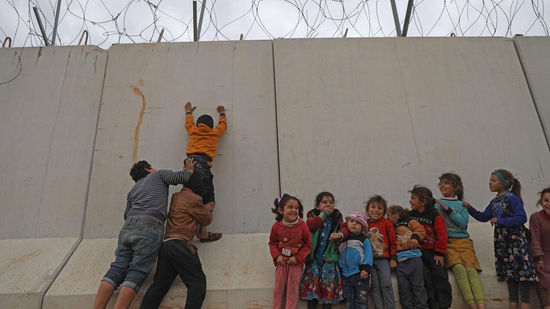 Fotografija: Otroški begunci, ujeti na severu Sirije, poskušajo preplezati zid, ki ga je Turčija postavila na meji, da bi preprečila prihod beguncev iz Sirije. FOTO: Aaref Watad/AFP