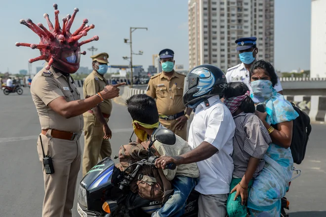 V Chennaiju policijski inšpektor Rajesh Babu, ki nosi čelado v obliki koronavirusoa, govori z družino na motornem kolesu na kontrolni točki med državno zaporo, ki jo je indijska vlada uvedla, kot preventivni ukrep proti koronavirusu . FOTO: Arun Sankar/Afp