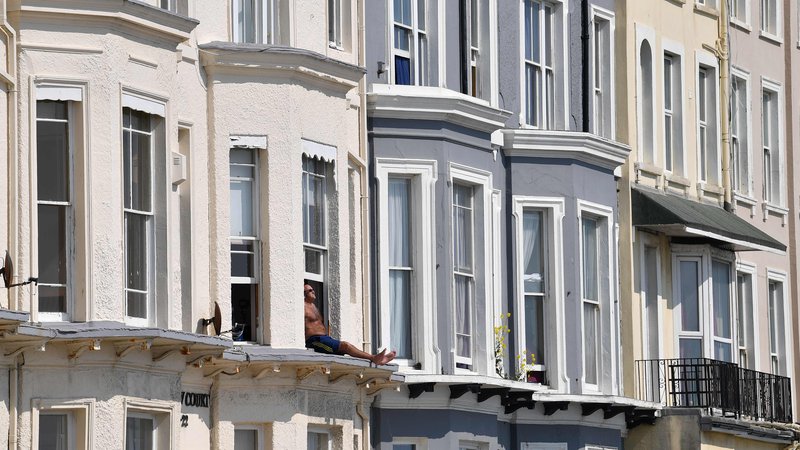 Fotografija: Moški se sonči na okenski polici svoje sobe v Hastingsu, na južni obali Anglije. Bolezen je prišla v osrčje britanske vlade, okužila je več kot 60.000 ljudi po vsej državi, umrlo pa jih je več kot 7.000. 8. aprila so poročali o največjem dnevnem številu 938 smrtnih žrtev. FOTO: Ben Stansall/Afp
 