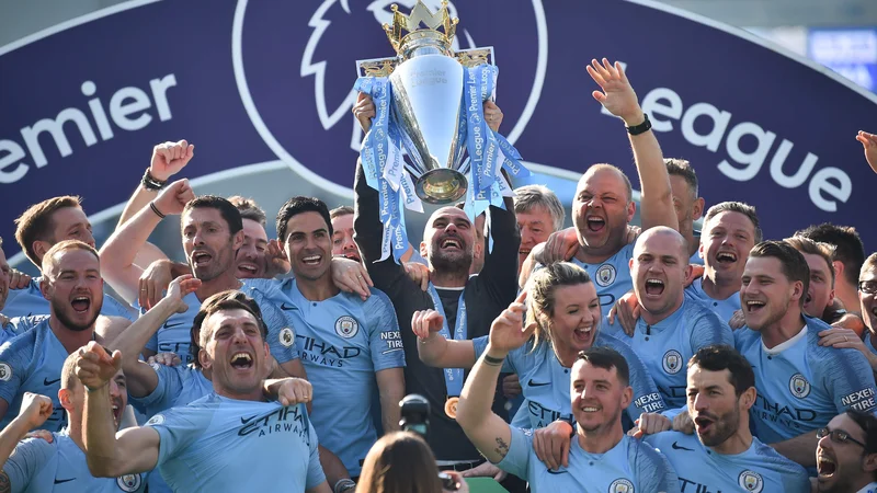 Fotografija: Strateg Manchester Cityja Pep Guardiola je 12. maja letos tako dvignil pokal za naslov zmagovalca premier league, obkrožen s svojimi nogometaši in njihovimi družinskimi člani. ManCity je prvi favorit za lovoriko tudi v sezoni, ki jo bodo odprli ta petek v Liverpoolu. FOTO: AFP