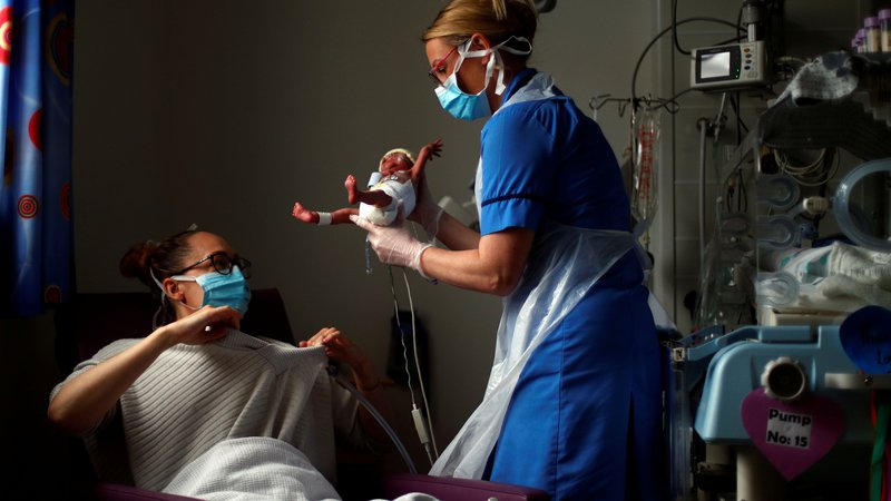 Fotografija: Na oddelku za intenzivno nego v porodnišnici v Burnleyu medicinska sestra Kirsty Hartley nosi nedonošenčka Thea h mami Kirsty Anderson. FOTO: Hannah Mckay/Afp
 