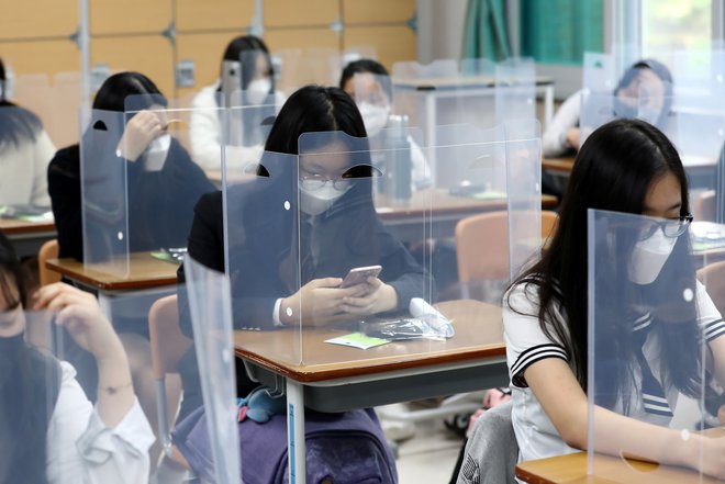 V Južni Koreji se je po dveh mesecih od zaprtja šol danes v šolske klopi spet vrnilo približno 440.000 dijakov zadnjih letnikov, ki bodo decembra opravljali sprejemne izpite na univerzah. Pouk so znova uvedli ob upoštevanju ukrepov socialnega distanciranja in večje higiene, dijakom pa pred vstopom v šolske stavbe merijo tudi telesno temperaturo. FOTO: Yonhap/Reuters