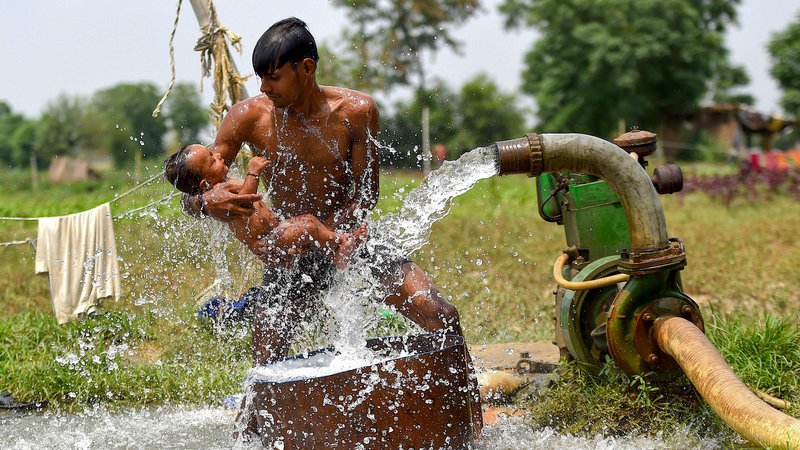 Fotografija: Moški hladi sina z vodo iz vodne cevi na polju na obrobju New Delhija na vroč poletni dan. FOTO: Money Sharma/Afp