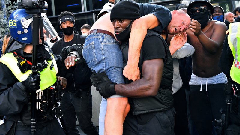 Fotografija: Na ulice britanske prestolnice so se podali nasprotniki rasizma in skrajno desne skupine. Med demonstracijami je protestnik pretepenega in poškodovanega udeleženca na rami odnesel proti varnostikom v bližini postaje Waterloo v Londonu. FOTO: Dylan Martinez/Reuters