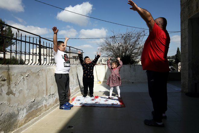 Življenje v času karantene: Victor Anton Sara iz Jeruzalema telovadi na terasi s tremi otroki. FOTO: Ammar Awad/Reuters