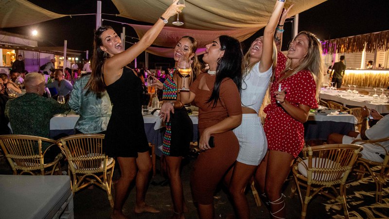 Fotografija: Ženske plešejo na terasi restavracije, ki se nahaja na plaži v mestecu Fregene blizu Rima. DJ zaman kriči v mikrofon naj si gostje nadenejo maske. Medtem ko se grožnja drugega vala koronavirusa širi v več evropskih državah, Italija poskuša sredi ferragoste (počitniški čas, ki izhaja še iz rimskih časov, danes imenovan veliki šmaren, ki se začne 15. avgusta) preprečiti nove okužbe. FOTO: Tiziana Fabi/Afp