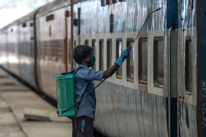 Sanitarni delavec med razkuževanjem vlaka v okviru priprav na ponovno odprtje železniške postaje po vladni odločitvi rahljanja ukrepov. FOTO: Arun Sankar/AFP