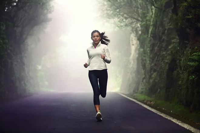 Woman running on road. Female runner jogging on mountain road training for marathon. Fit girl fitness athlete model exercising outdoor.