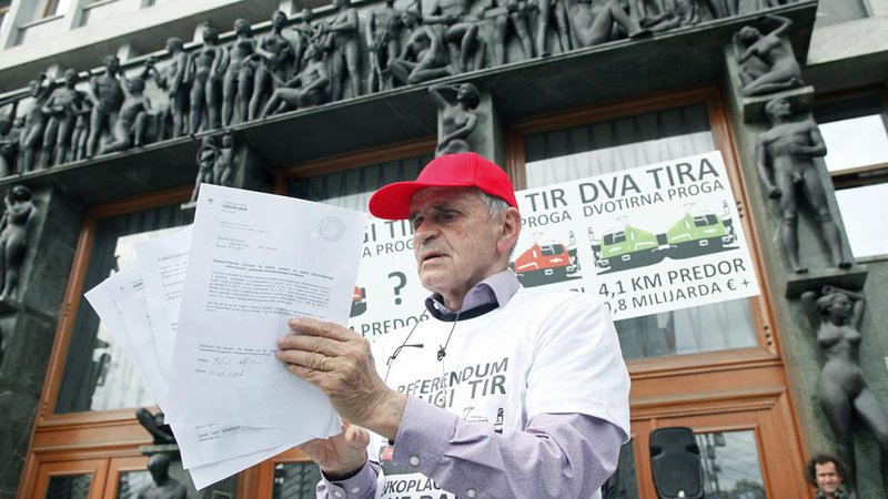 Fotografija: Vili Kovačič pred parlamentom z podpisi za zaustavitev gradje dugega tira. FOTO: Mavric Pivk/Delo