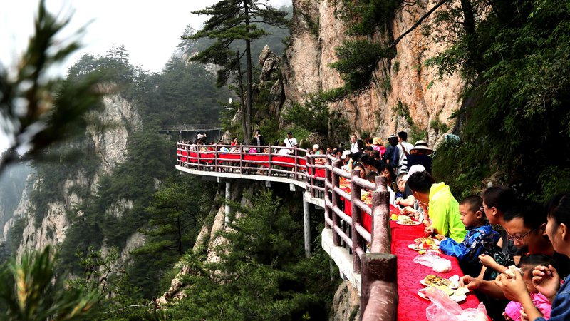 Fotografija: Turisti med banketom ob robu pečine na 2000 metrov visoki gori Laojun na Kitajskem. S tovrstno promocijo želijo domačini privabiti čim več turistov. Foto - Afp