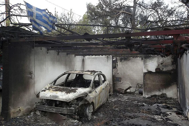 V požaru poškodovana grška zastava kot simbol grške ognjene tragedije. FOTO: AP
