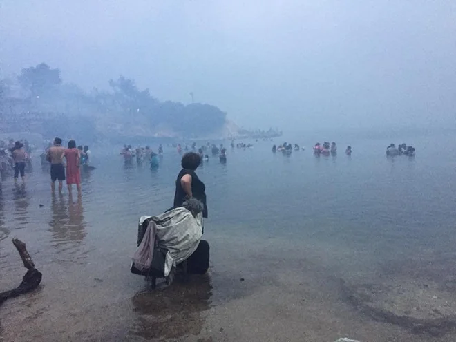 Lokalni prebivalci in turisti so se v Mati, tako kot marsikje drugje, kjer je zagorelo, pred ognjem zatekli k morju. FOTO: Reuters