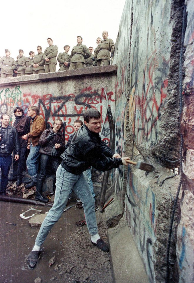 Na sliki je protestnik, ki 11. novembra 1989, dva dni po padcu berlinskega zidu, uničuje mejnik, ki je 28 let delil vzhodni in zahodni del nemške prestolnice. Z vrha zidu ga opazujejo mejni pazniki z vzhodnega predela. FOTO: Stringer/Reuters