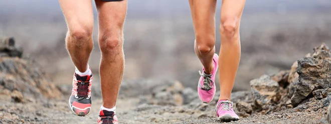 Trail running - close up of runners shoes and legs of athletes exercising and cross-country running outside on rocks on volcano path. Woman and man lower section closeup.