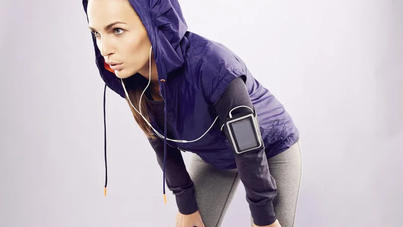 Fotografija: Young caucasian woman taking breath after jogging. Female athlete resting with hands on knees and looking away over grey background