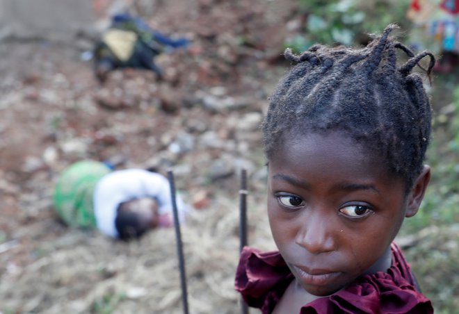 Dekle stoji pred trupli ubitih žensk v kraju Paida na severu Demokratične republike Kongo. FOTO: Goran Tomasevic/Reuters