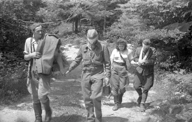 Bolničar in bolničarka vodita ozdravela ranjenca z zavezanimi očmi iz bolnice do javke, od koder se bosta vrnila v enoto; poletje 1944. Foto dr. Janez Milčinski/Muzej novejše zgodovine Slovenije