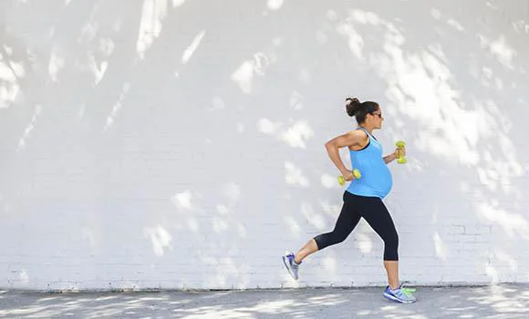 Young pregnant woman jogging down sidewalk in city.