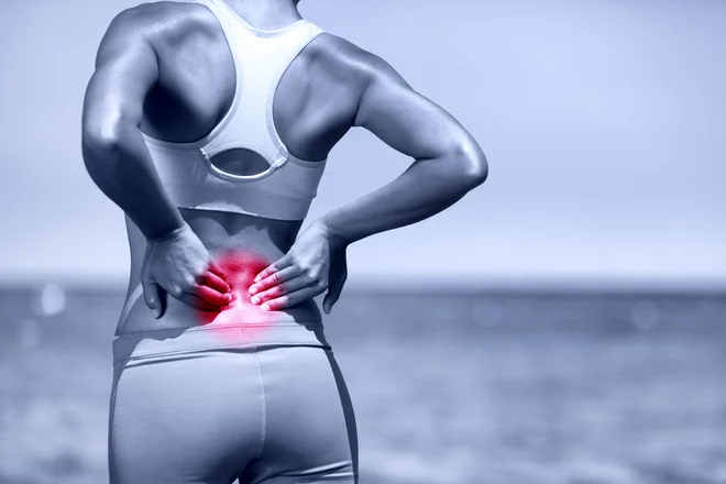 34943050 - back pain. athletic running woman with back injury in sportswear rubbing touching lower back muscles standing on road outside.