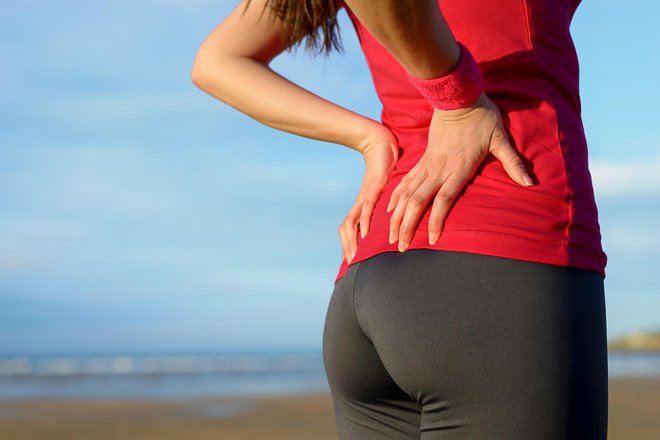 Female athlete lower back painful injury. Caucasian fitness girl gripping her lowerback because sport injury after exercising and running.