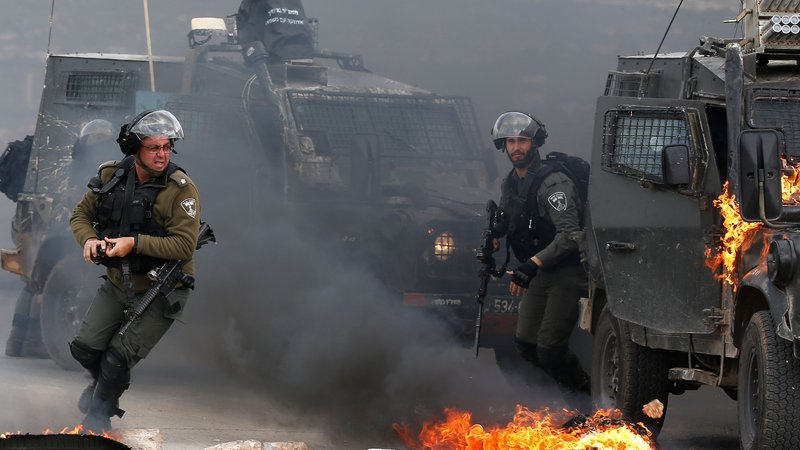 Fotografija: Na obrobju Ramale v zasedenem Zahodnem bregu se izraelski vojaki, zadolženi za varovanje meje, umikajo iz gorečega vojaškega vozila med spopadi s palestinskimi demonstranti, ki so odpravili na ulice v podporo palestinskim zapornikom v izraelskih zaporih. Foto Abbas Momani Afp