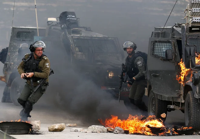 Na obrobju Ramale v zasedenem Zahodnem bregu se izraelski vojaki, zadolženi za varovanje meje, umikajo iz gorečega vojaškega vozila med spopadi s palestinskimi demonstranti, ki so odpravili na ulice v podporo palestinskim zapornikom v izraelskih zaporih. Foto Abbas Momani Afp