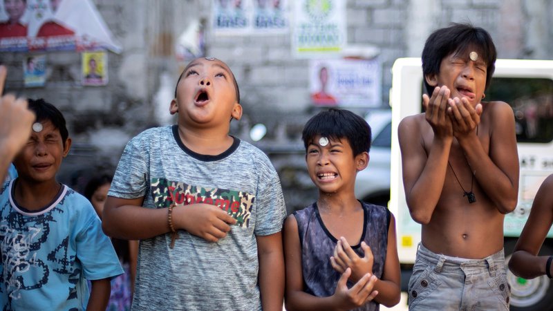 Fotografija: V Manili so se otroci v okviru posta na dan svete Rite iz Casie pomerili v različnih spretnostnih igrah. Na fotografiji so morali kovanec iz čela brez rok kar najhitreje spraviti v usta. Foto Noel Celis Afp